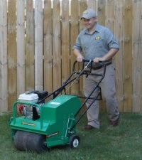Green Bee Lawn Care technician walking on grass with spiked shoes for lawn aeration 